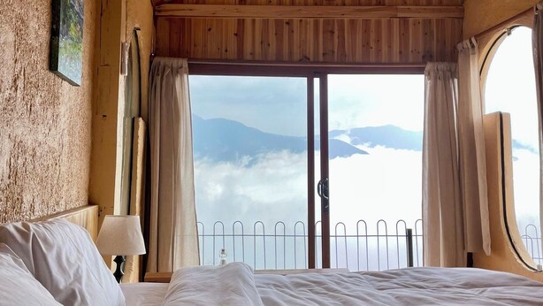 Un dormitorio con techo de madera, una cama grande, una ventana con cortinas y vistas a montañas.