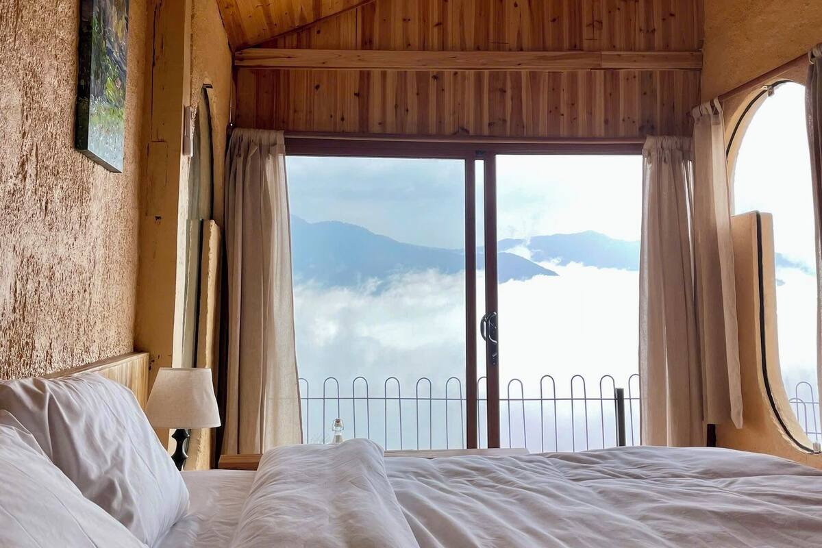 Une chambre avec un plafond en bois, un grand lit, une fenêtre avec des rideaux et une vue sur les montagnes.