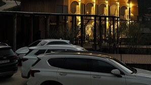 Un edificio tradicional con tejado de tejas, fachada de madera y una serie de aberturas en arco. Hay coches aparcados frente al edificio.