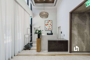 A reception area with a reception desk, a potted plant, a hanging light fixture, and a door with a logo. - Downtown Stay | Pools, Gym & Rooftop Views (Miami)