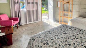 Una habitación con cama, una silla, un estante de madera y vistas al exterior.