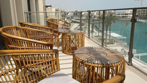 Ein Balkon mit Korbmöbeln, einem Glastisch und Blick auf einen Yachthafen.