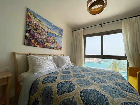 A bedroom with a bed, a painting, a window with a view, and a hanging light fixture. - Chalet 3 Bedrooms LR - 404 in Marassi (El Alamein)