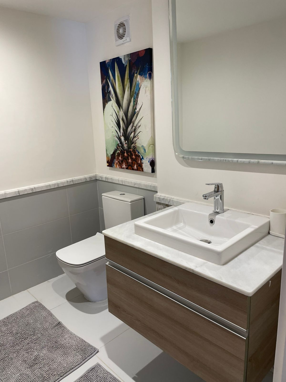 A modern bathroom with a white toilet, a sink with a mirror, and a painting of a plant on the wall.