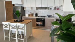 Eine moderne Küche mit weißen Schränken, einer Holztischinsel, weißen Stühlen, einem Kühlschrank, einem Herd und einem Backofen.