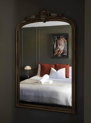 A bedroom with a large mirror, a bed with white linens, red pillows, and a painting on the wall. - Art Deco Penthouse Retreat | Luxury on 2 levels (Melbourne)