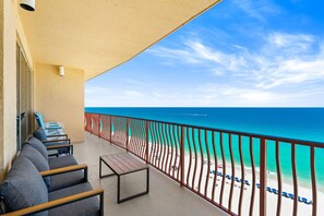Ein Balkon mit Blick auf den Strand, eine Reihe von Stühlen und ein Tisch.