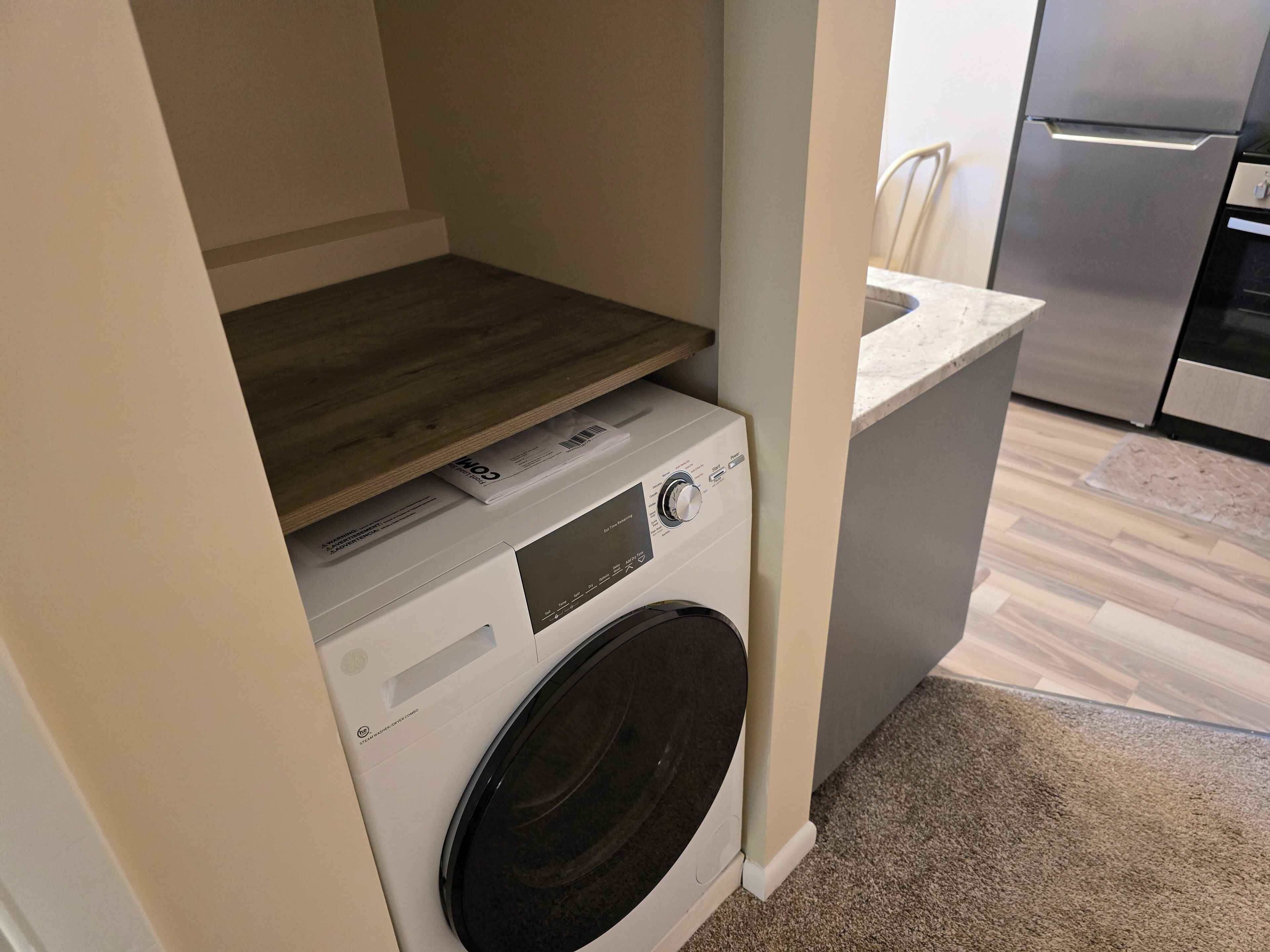 A compact laundry area with a washing machine, a drying rack, and a built-in countertop.