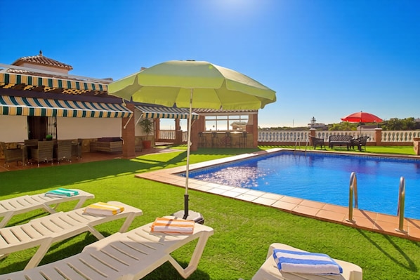 A swimming pool with lounge chairs and umbrellas, surrounded by a well-maintained lawn and a building with a tiled roof. - Sara Sol in Frigiliana (Frigiliana)