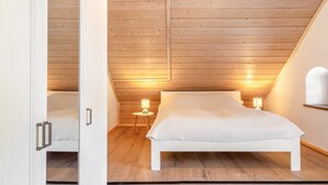 A bedroom with a sloped ceiling, wooden walls, a white bed, and two bedside lamps. - Apartment 'Fewo Edelweiss' with Private Sun Terrace and Wi-Fi (Breitenberg)
