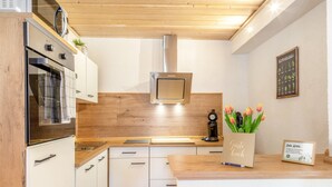 A modern kitchen with wooden cabinets, a built-in oven, a stainless steel range hood, and a wooden countertop. - Apartment 'Fewo Edelweiss' with Private Sun Terrace and Wi-Fi (Breitenberg)