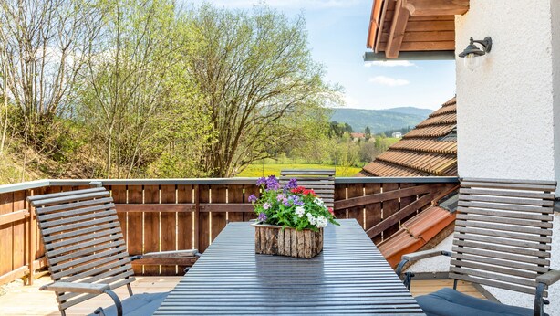 Een terras buiten met een houten tafel, twee banken en een bloempot.