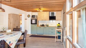 Een keuken met houten kastjes, een eettafel met stoelen en uitzicht door een raam.