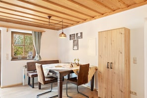 Un coin repas avec un plafond en bois, une table entourée de chaises, une fenêtre avec des rideaux et un buffet en bois.