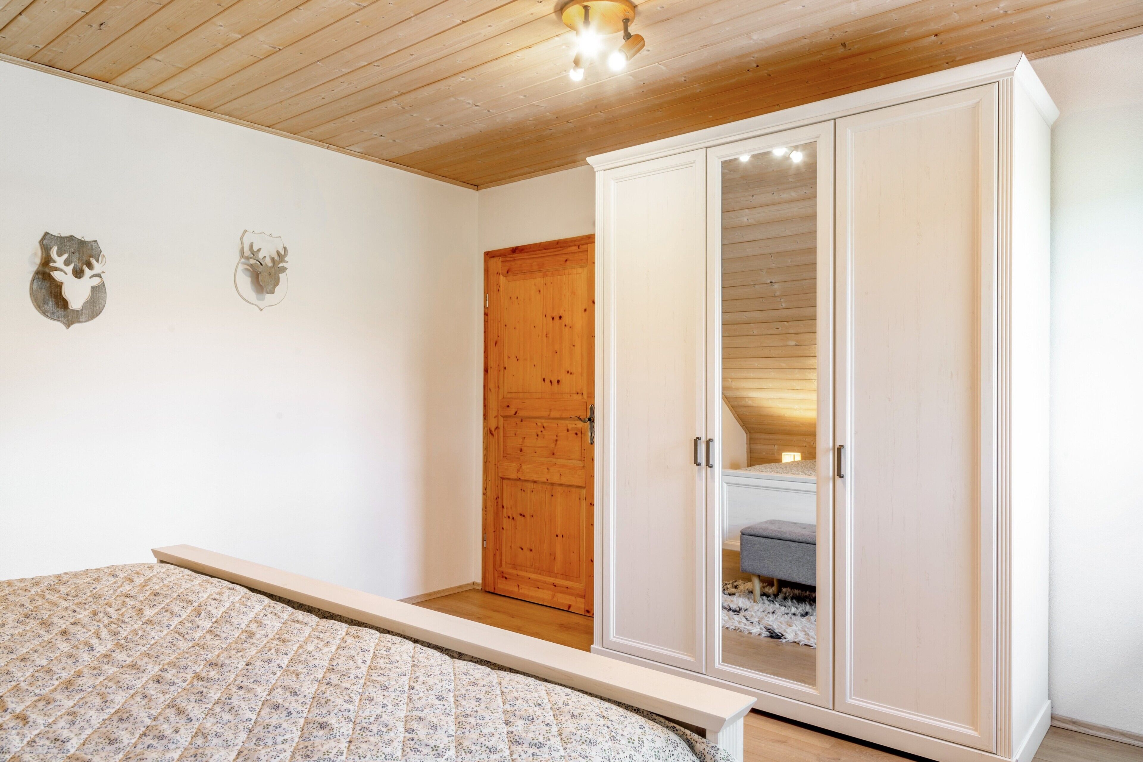 A bedroom with a bed, a wardrobe, a wooden door, and two wall decorations.