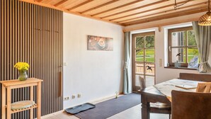 Een houten plafond, een eettafel met stoelen, een vaas met bloemen en een schilderij aan de muur.