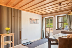 Techo de madera, una mesa de comedor con sillas, un jarrón con flores y un cuadro en la pared.