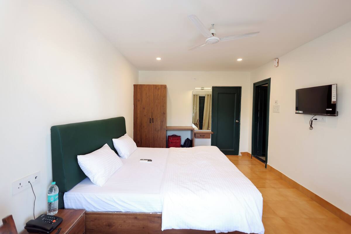 Ett hotellrum med en säng, ett skrivbord, en stol, en TV, en garderob och en takfläkt.