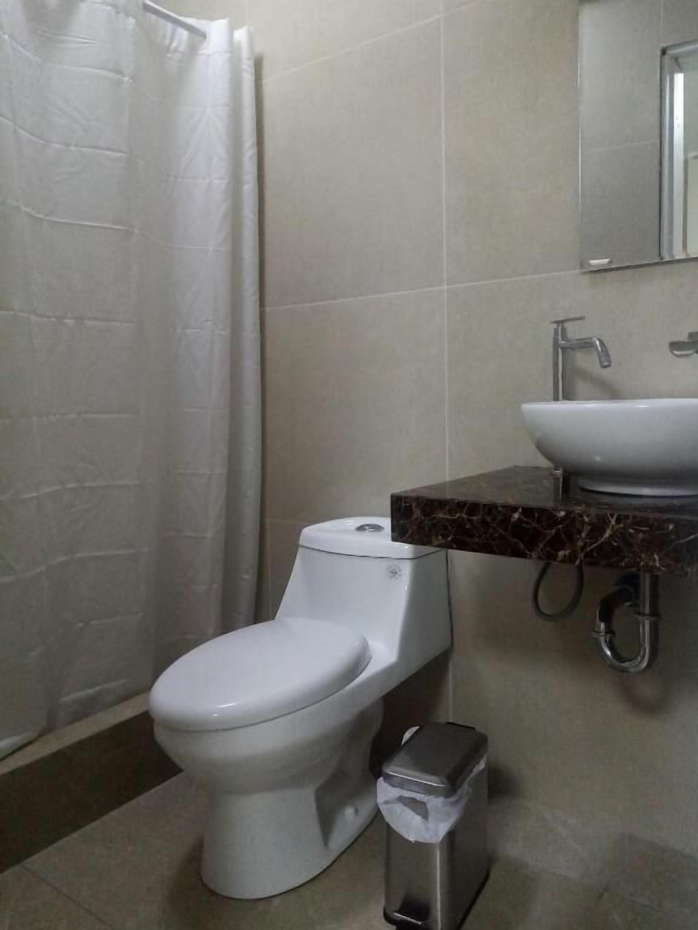 A bathroom with a toilet, a sink, and a trash bin.