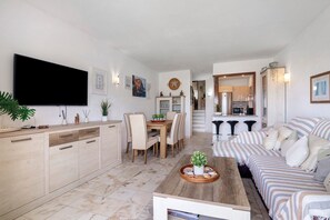 A modern living room with a flat-screen TV, a dining area with a wooden table and chairs, and a striped sofa.