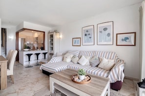 Un salon avec un canapé à rayures, une table basse agrémentée d’objets décoratifs, un coin cuisine avec un bar et des œuvres d’art encadrées accrochées au mur.