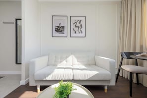 Een moderne woonkamer met een lichtkleurige bank, een ronde salontafel met een plant, en twee ingelijste kunstwerken aan de muur.
