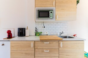 Eine Küche mit Holzausstattung, einer Mikrowelle, einer Kaffeemaschine, einem Spülbecken und einem Schneidebrett.