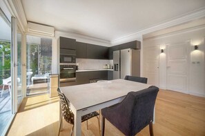 Eine moderne Küche mit Einbaugeräten, ein Essbereich mit Tisch und Stühlen sowie eine Glastür, die zu einem Sitzbereich im Freien führt.