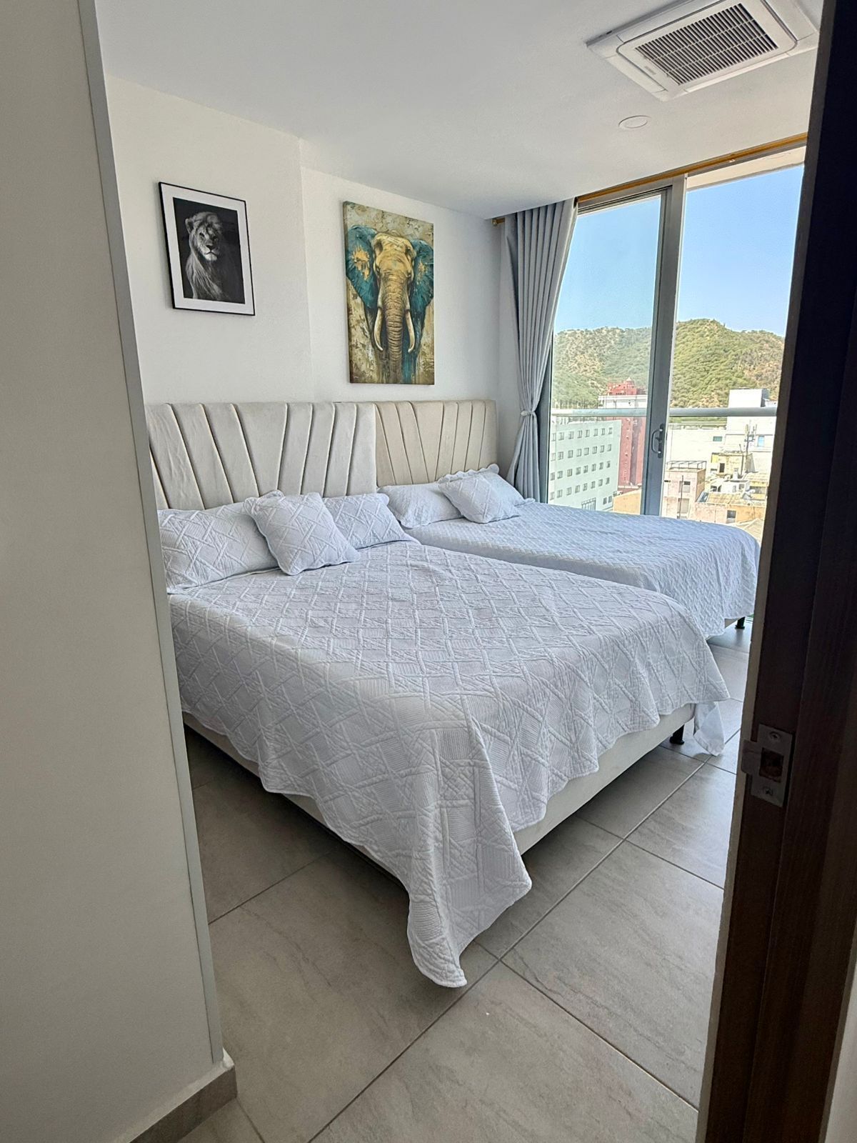 Une chambre avec deux lits, une grande fenêtre et des  œuvres d’art accrochées au mur.