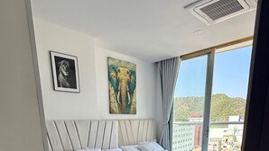 Et soveværelse med to senge, et stort vindue og billedkunst på væggen.