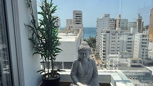 En Buddha-statue på en balkon med en potteplante og en lille stentøft.