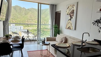 Un appartement moderne comprenant un coin repas, une cuisine et de grandes portes-fenêtres coulissantes donnant sur un balcon avec vue sur les collines.