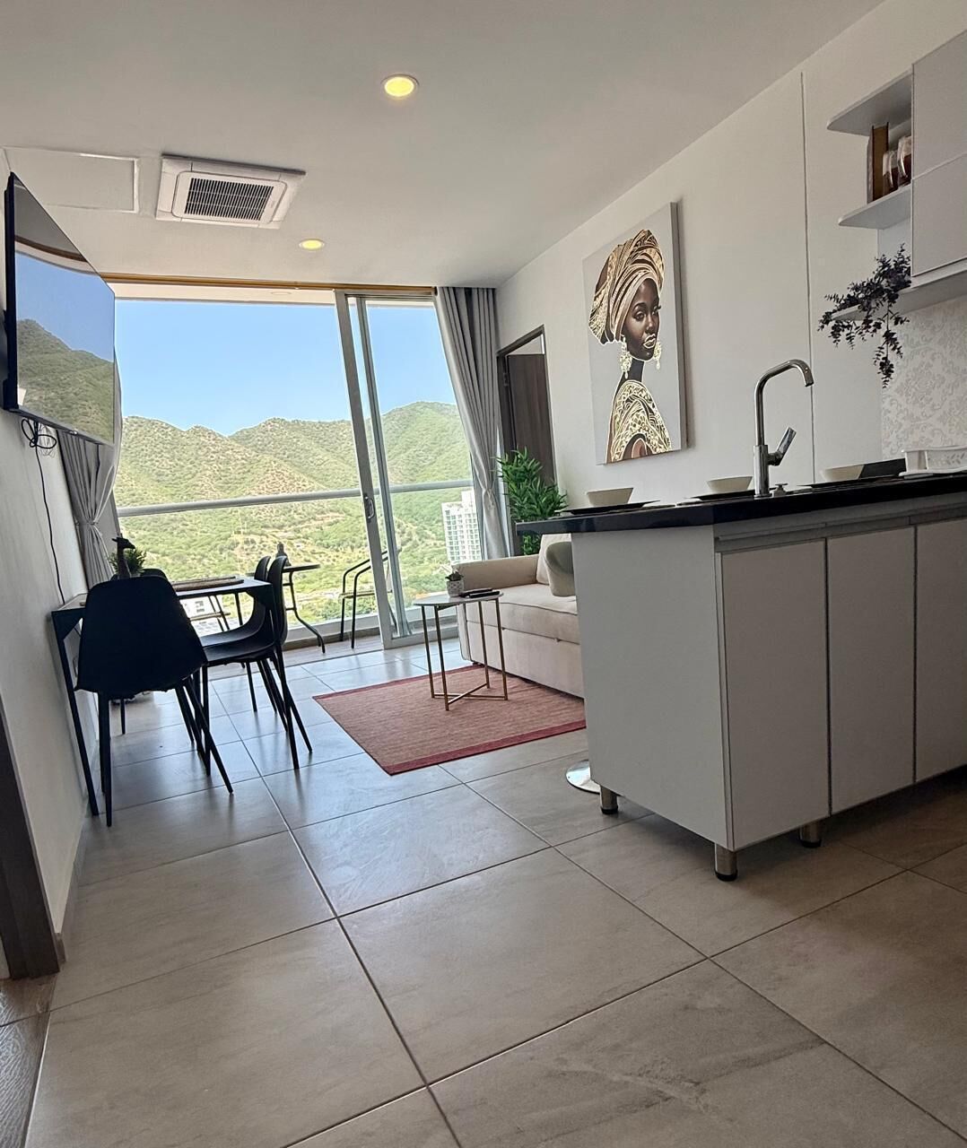 Une cuisine moderne dotée d’un grand îlot central, d’un coin repas avec des chaises et offrant une vue sur un paysage montagneux grâce à de grandes fenêtres.
