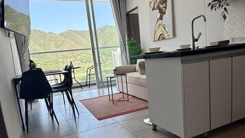 Una cocina moderna con una isla grande, un comedor con sillas y vistas a un paisaje montañoso a través de amplios ventanales.
