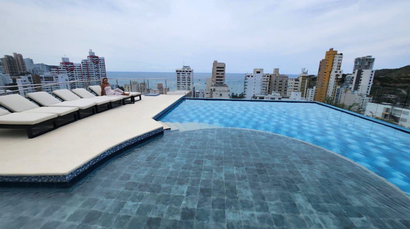 Une piscine à débordement située sur le toit, avec des chaises longues, une terrasse carrelée et une vue sur les gratte-ciel de la ville.