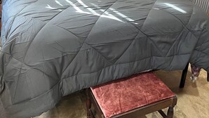 Ein Bett mit einer gesteppten, grauen Bettdecke, zwei Kissen und einem hölzernen Kopfteil.