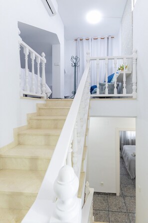 Eine Treppe mit weißen Balustraden führt zu einer Empore mit einem Bett.