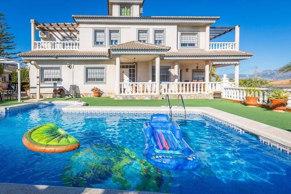 Ein zweistöckiges Haus mit Schwimmbad, überdachter Terrasse und gepflegtem Rasen.