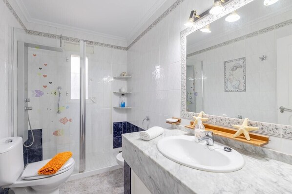 A modern bathroom with a glass shower enclosure, a white toilet, a marble sink, and a large mirror.