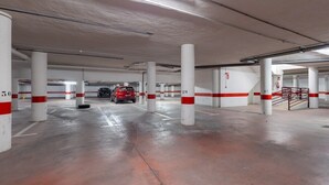 A multi-level parking garage with white pillars marked with red and white stripes, and a red car parked in the distance. - Feel at Home by Fidalsa (Torrevieja)