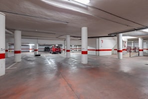 Eine mehrgeschossige Parkgarage mit weißen Säulen, die mit rot-weißen Streifen gekennzeichnet sind, und ein rotes Auto, das in der Ferne geparkt ist.