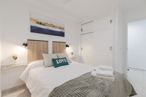 A bedroom with a bed, a painting, two bedside tables, and a white door. - Feel at Home by Fidalsa (Torrevieja)