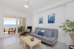 A living room with a sofa, a coffee table, a chair, and a potted plant. There is a sliding glass door leading to a balcony. - Feel at Home by Fidalsa (Torrevieja)