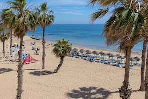 Ein Strand mit Palmen, einem Spielplatz und Strandsonnenschirmen.