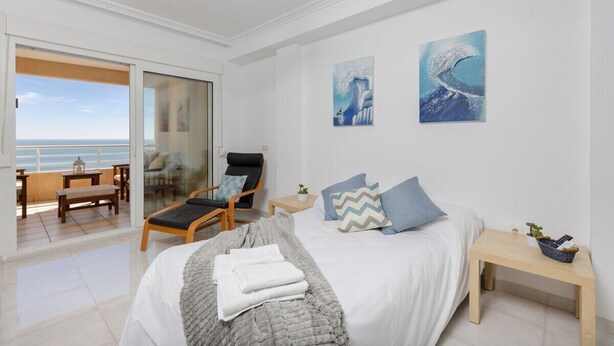 A bedroom with a bed, a chair, a small table, and a view of the ocean. - Feel at Home by Fidalsa (Torrevieja)