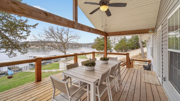 Un terrazzo in legno con tavolo e sedie, una ventola a soffitto e vista su un lago.