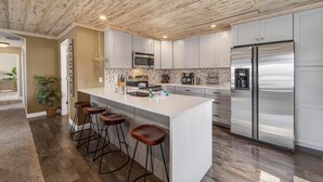 Una cucina moderna con isola centrale, sgabelli da bar, elettrodomestici in acciaio inossidabile e una parete di fondo con decorazione a spina di pesce.