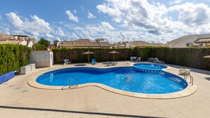 En pool med en böjd design, omgiven av solstolar och parasoller, med utsikt över bostadshus i bakgrunden.