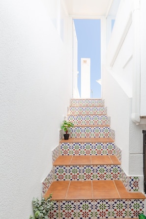 Eine enge Treppe mit bunten, gemusterten Fliesen und einem Blumentopf auf der ersten Stufe.