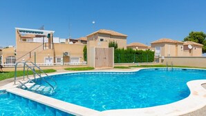 A swimming pool with a clear blue water, surrounded by buildings with tiled roofs and a fenced area. - Fidalsa Summer Breeze (Orihuela)